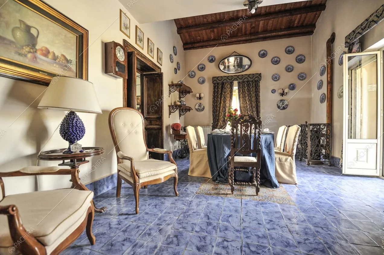 Sedie d'epoca in legno e stoffa, quadri e piatti appesi alle pareti e piastrelle blu
