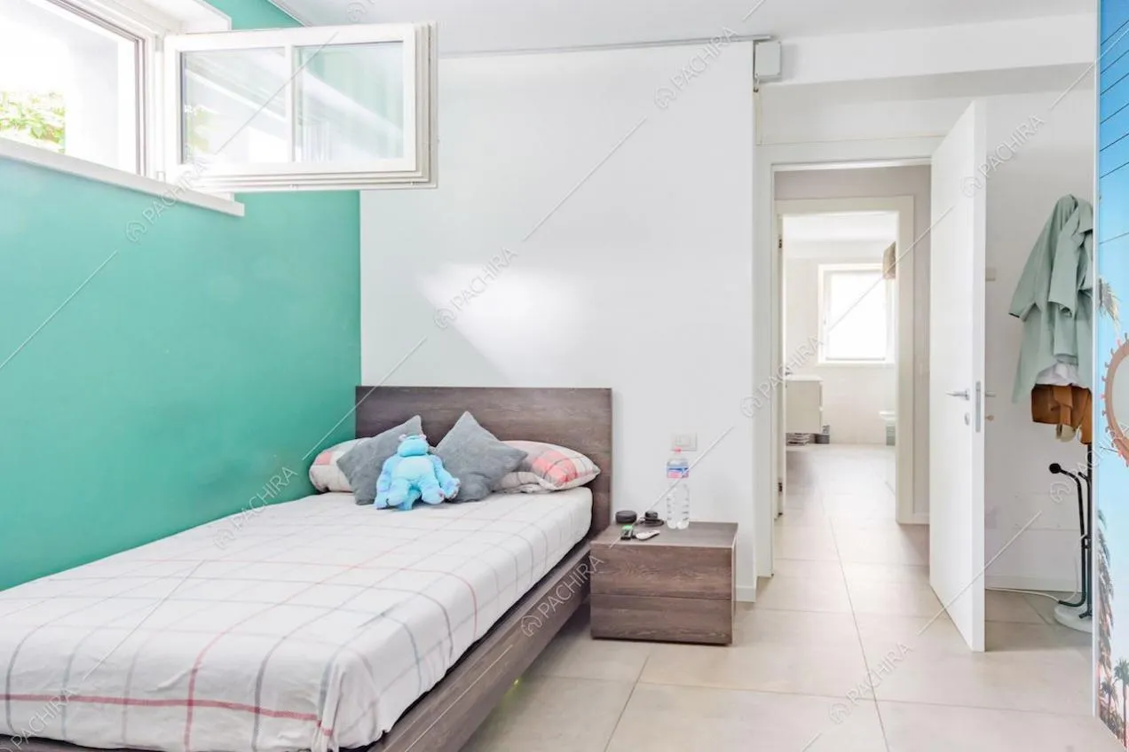 Letto singolo nella camera con parete verdeacqua e pavimento in piastrelle