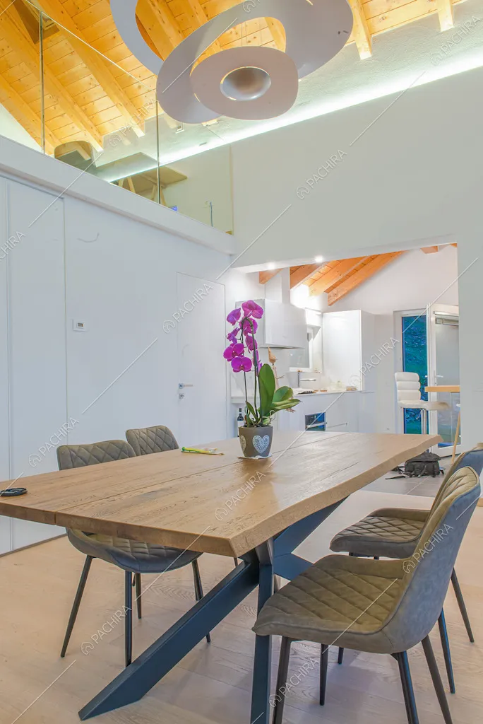 Tavolo da pranzo con piano in legno nell'open space con lampadario bianco di design, pareti bianche e vista sulla cucina