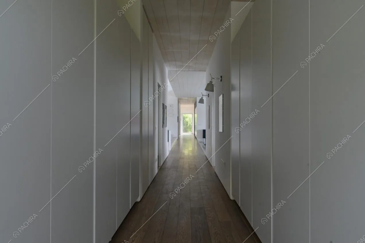 Lungo corridoio con armadi bianchi a muro, pavimento in parquet e soffitto bianco in legno