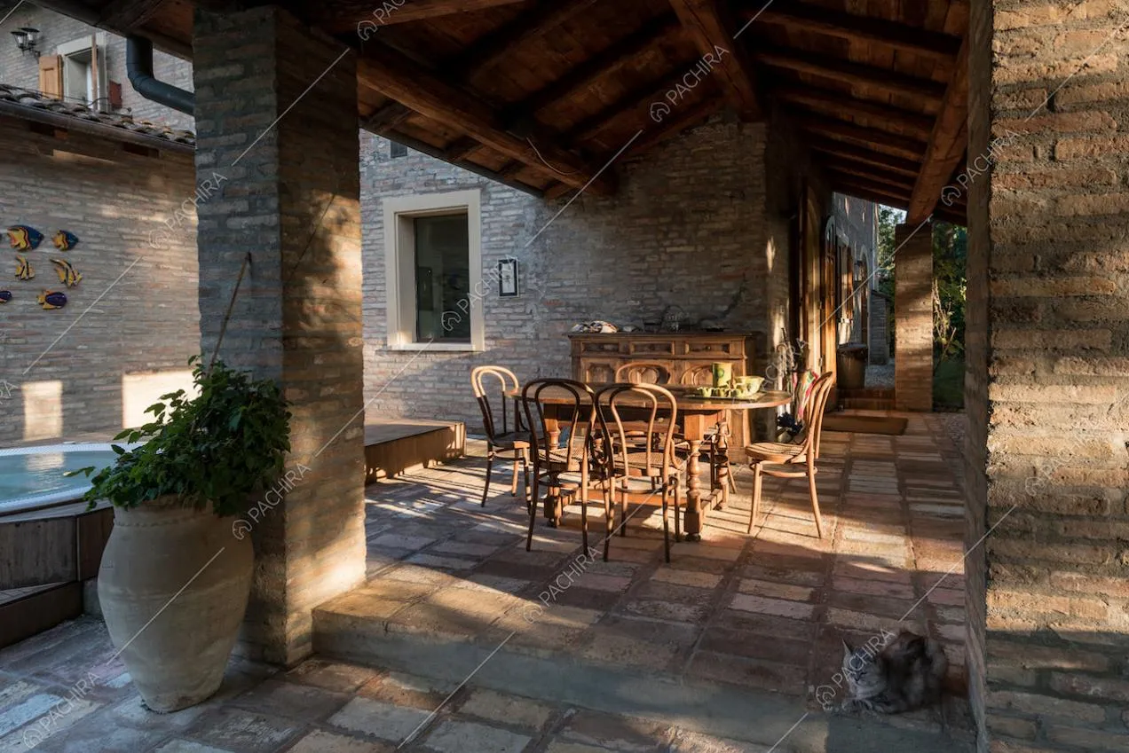 Veranda con soffitto in travi in legno a vista, pavimento in pietra, vasca e tavolo da pranzo