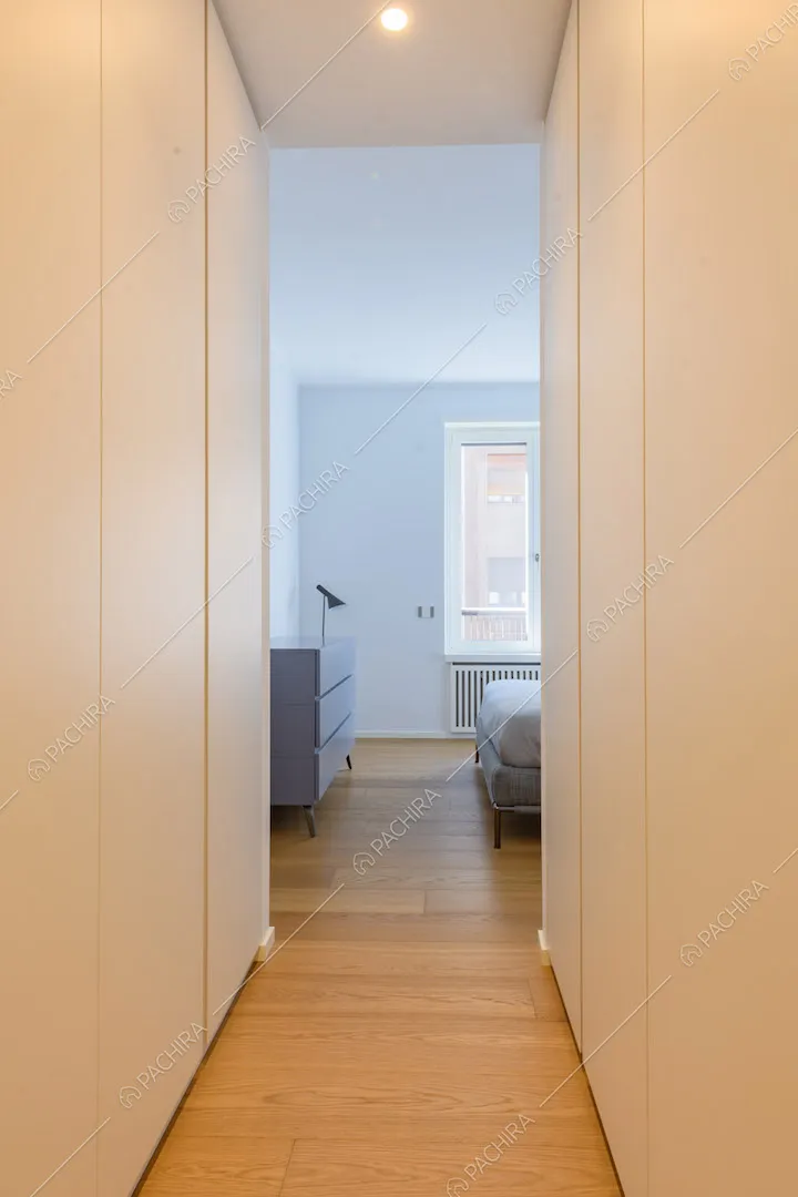Lungo corridoio con armadi a muro, pavimento in parquet e vista sulla camera da letto matrimoniale