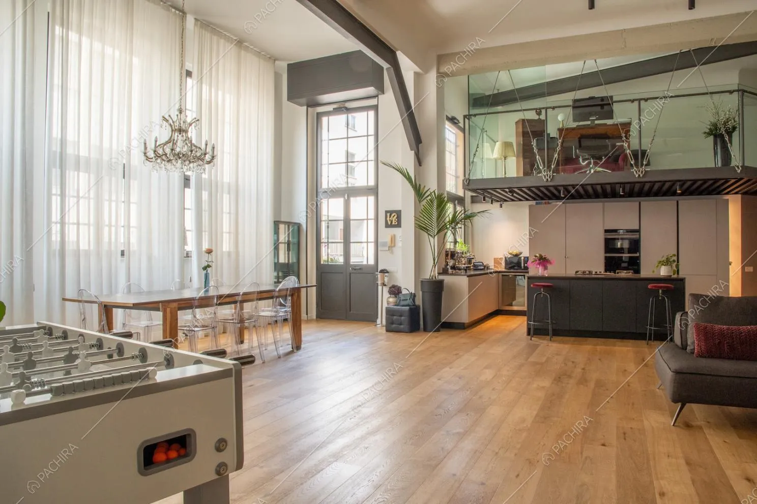 Soggiorno con ampie vetrate in stile industriale, soppalco con balaustra in vetro e cucina a vista