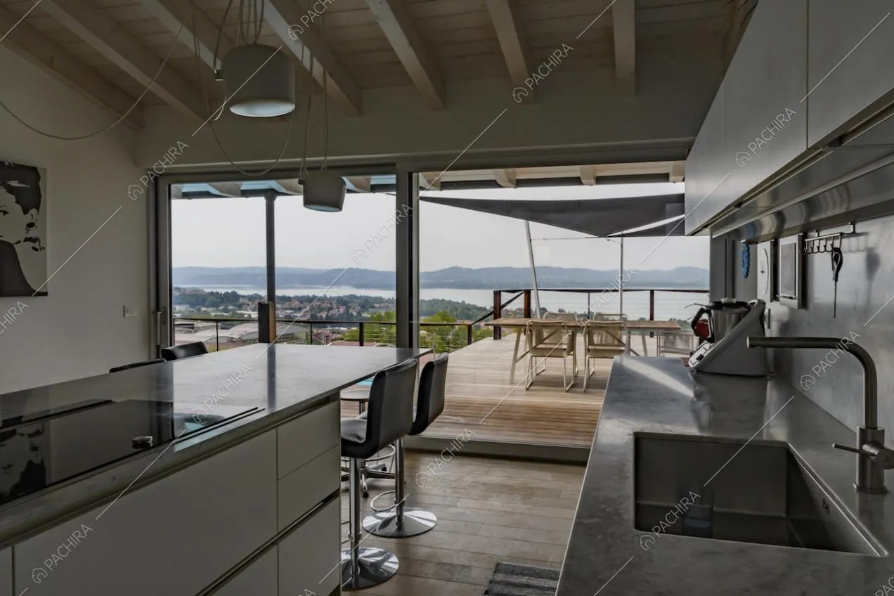 Cucina a isola con piano in marmo, fornelli a induzione, sgabelli e vista sulla terrazza tramite le vetrate