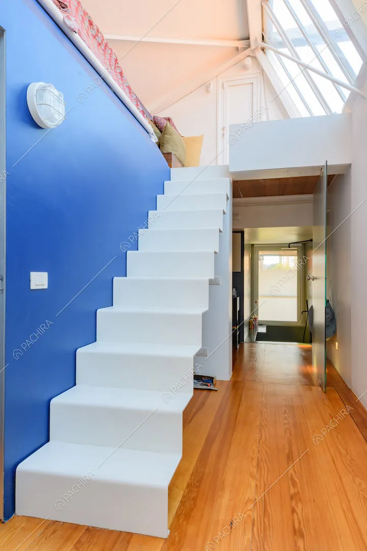 Scale bianche per accedere al soppalco, pavimento in parquet e parete blu