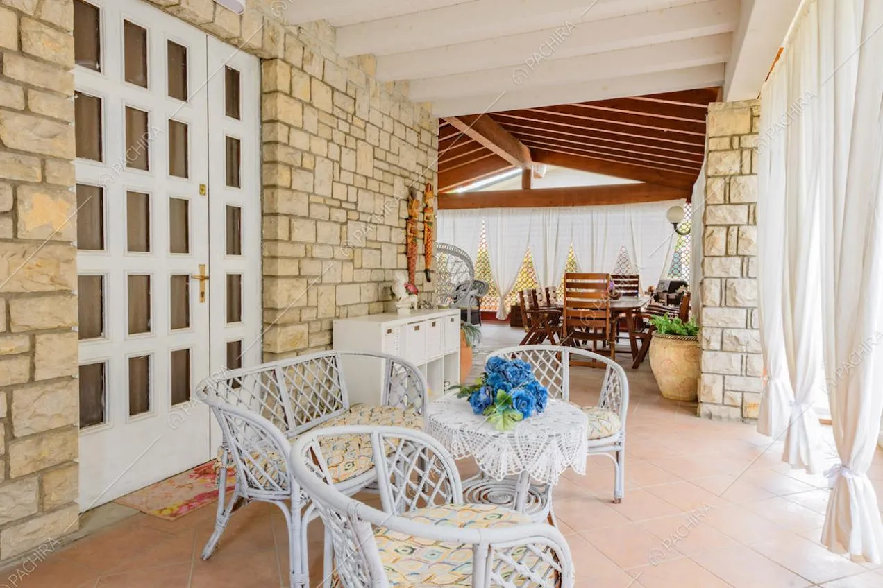 Poltrone e divano nella veranda con tende bianche e travi a vista