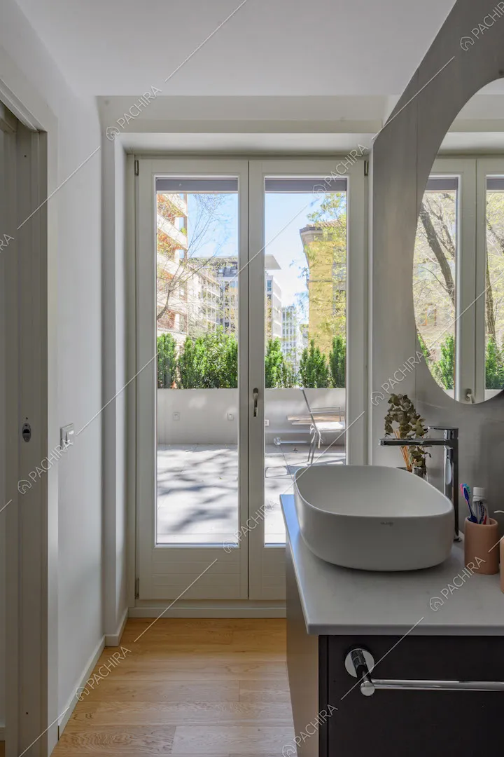 Luminoso bagno con parete grigia, pavimento in parquet e porta-finestra