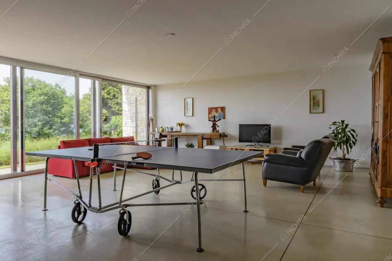 Sala con pavimento in cemento lisciato, con divani, tavolo da ping pong e pareti bianche