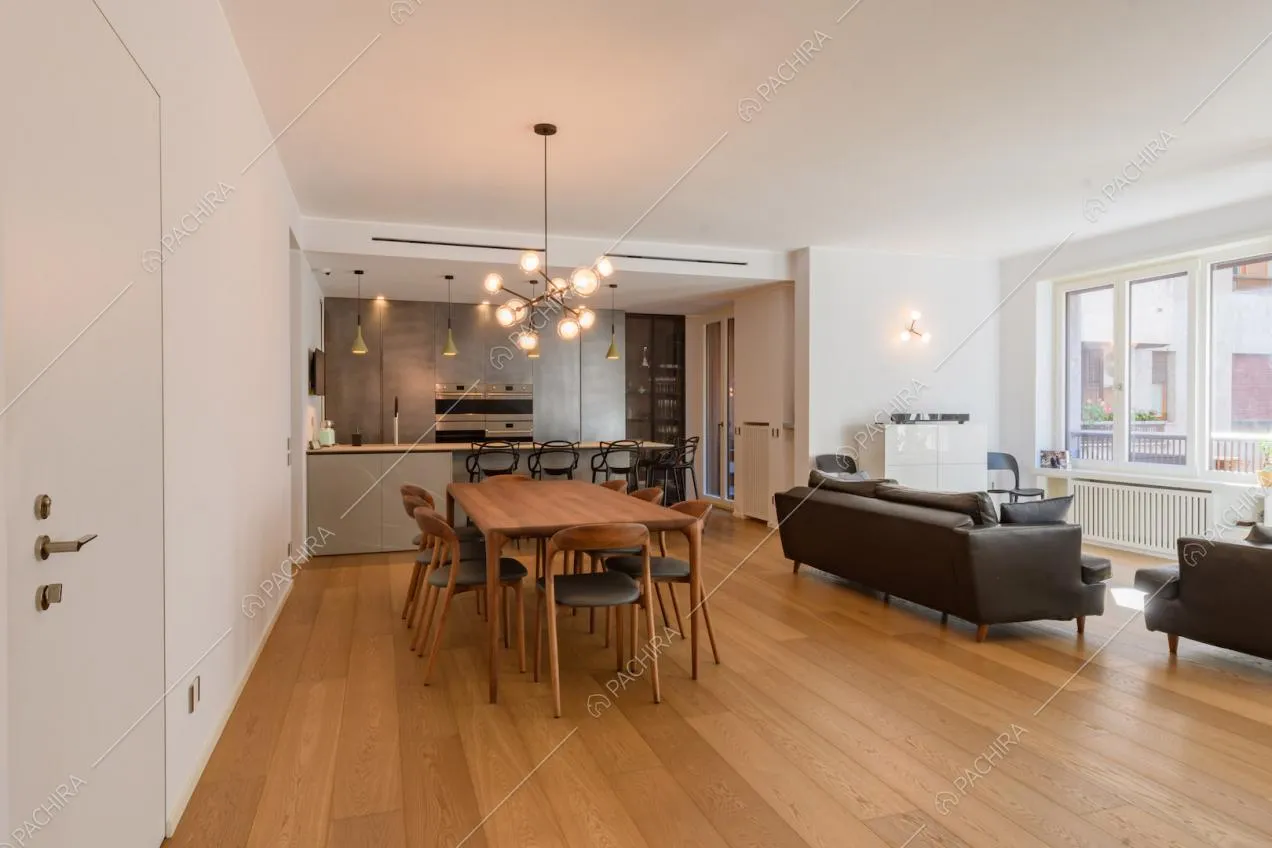 Ampia zona living con pareti bianche, pavimento in parquet e cucina a vista con penisola