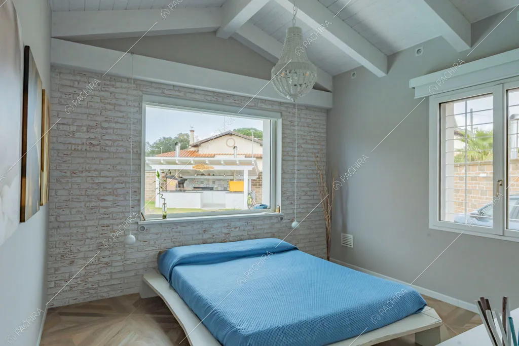 Camera da letto matrimoniale con parete in mattoni a vista della villa Colchito, location in stile contemporaneo a Roma