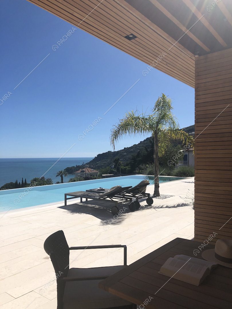 Dal tavolo da pranzo sulla veranda con soffitto in travi in legno, vista sulla piscina e sul mare