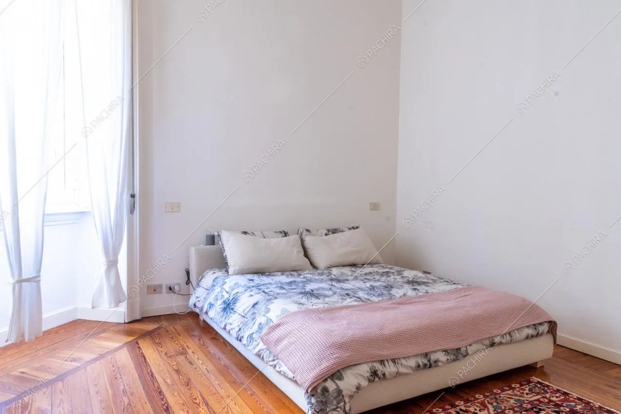 Letto matrimoniale in una luminosa camera da letto con pavimento in parquet a listoni