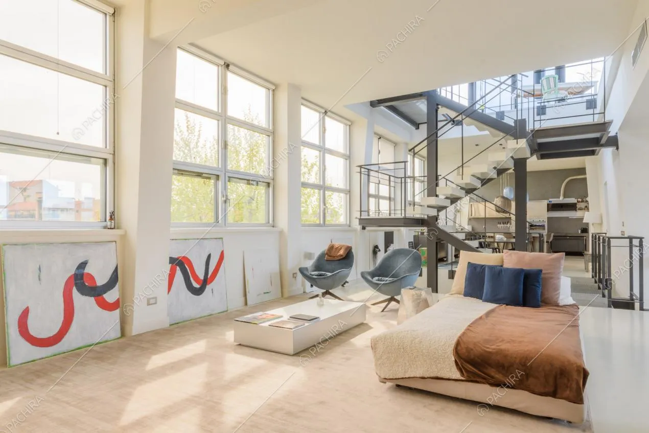 Luminosa zona living con grandi vetrate in stile industriale e vista su scale e cucina