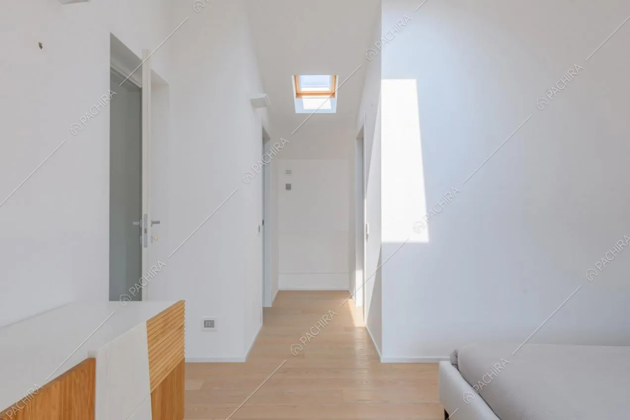 Grande camera da letto matrimoniale con lucernario, pareti bianche e pavimento in parquet