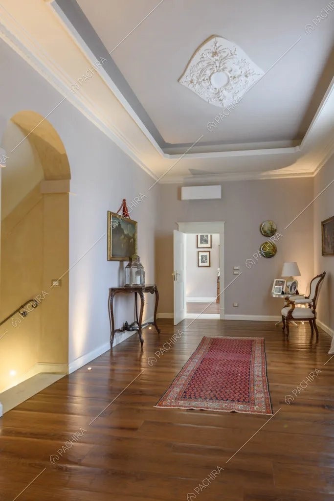 Ampio corridoio con pavimento in parquet, boiserie sul soffitto e vista sulle scale