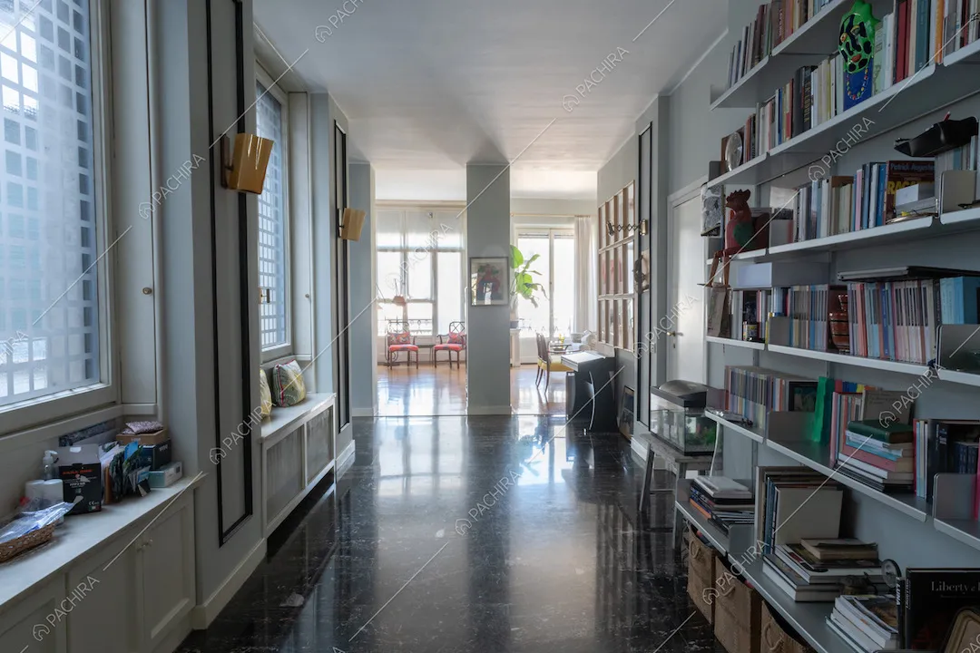 Corridoio con pavimento nero in piastrelle illuminato dalle ampie vetrate e vista sulla sala