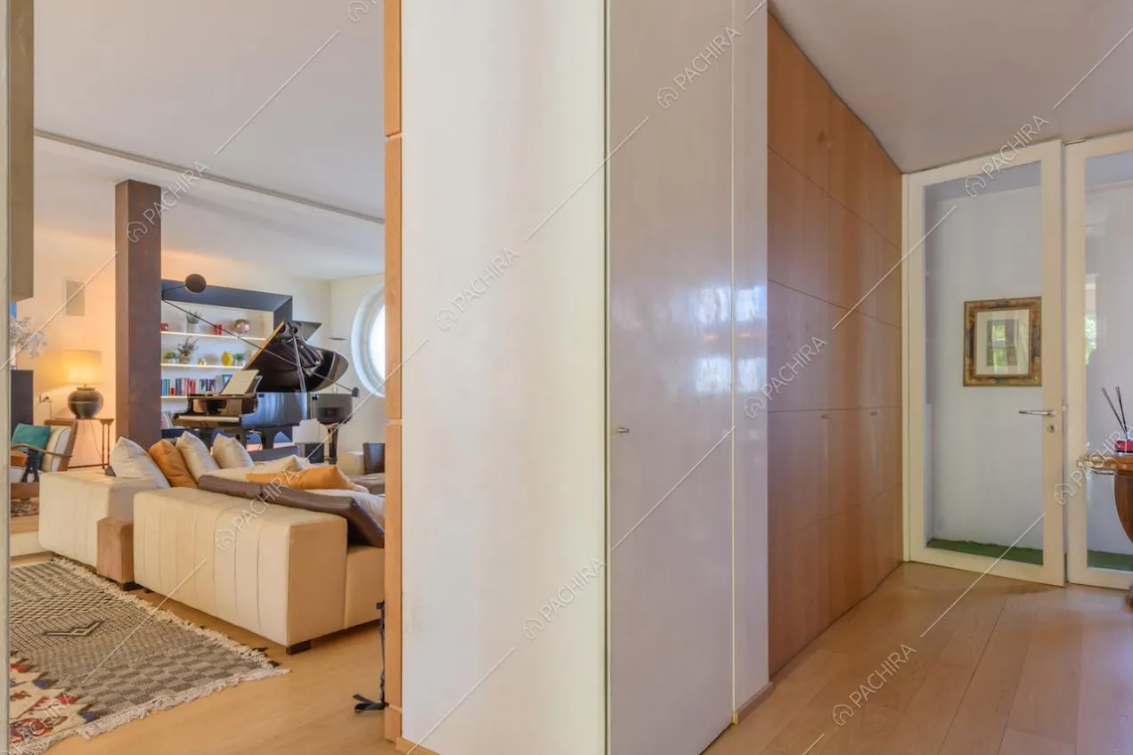 Vista sulla zona living dal corridoio con pavimento in parquet e porta a vetri