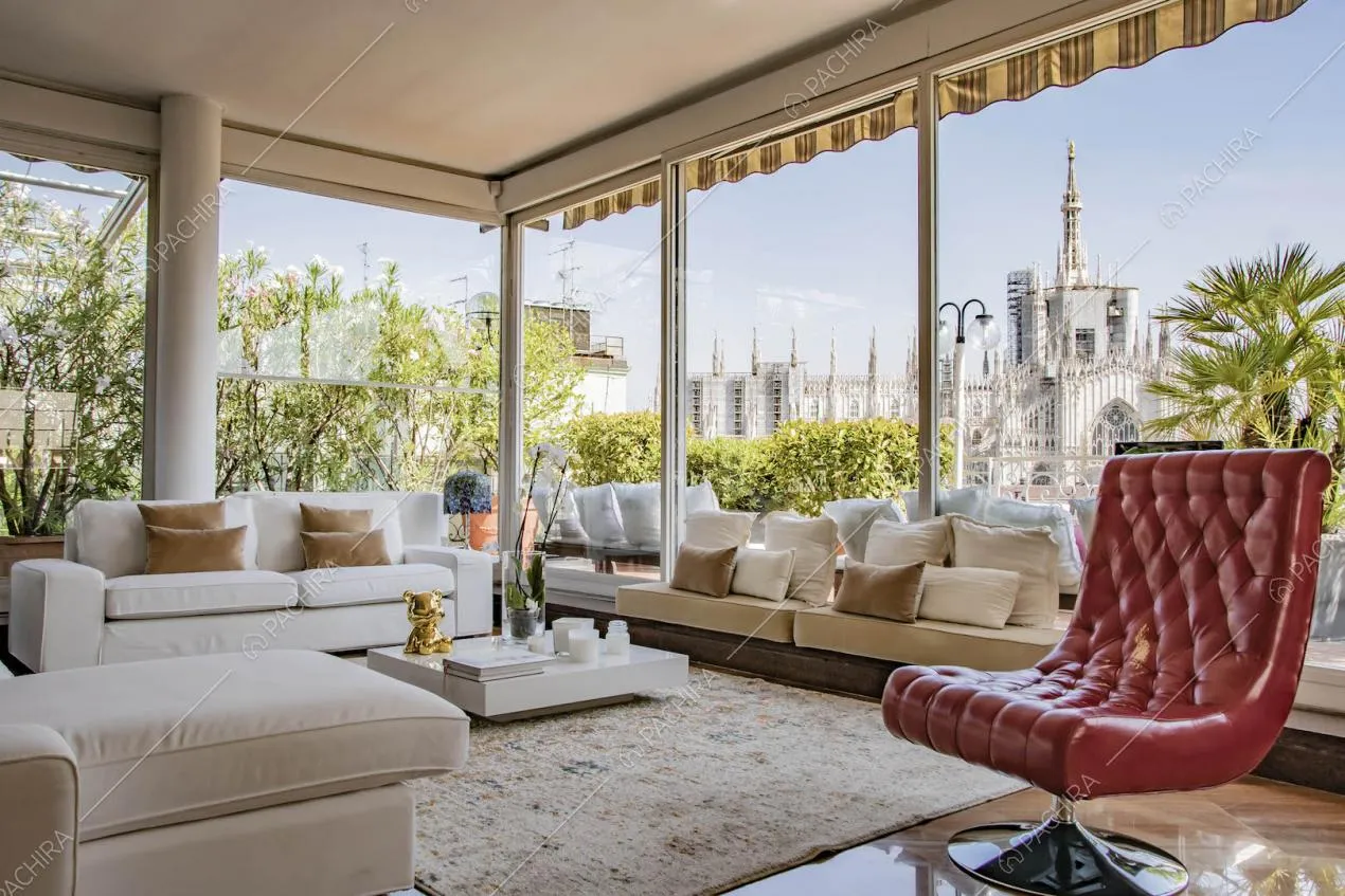 Ampia zona living con divani bianchi e vetrate che si affacciano sul Duomo di Milano