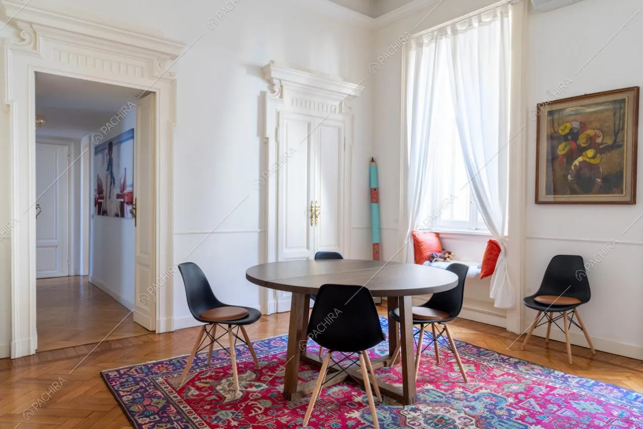 Tavolo da pranzo in legno e sedie nere nella sala con pavimento in parquet a spina di pesce e pareti bianche con boiserie