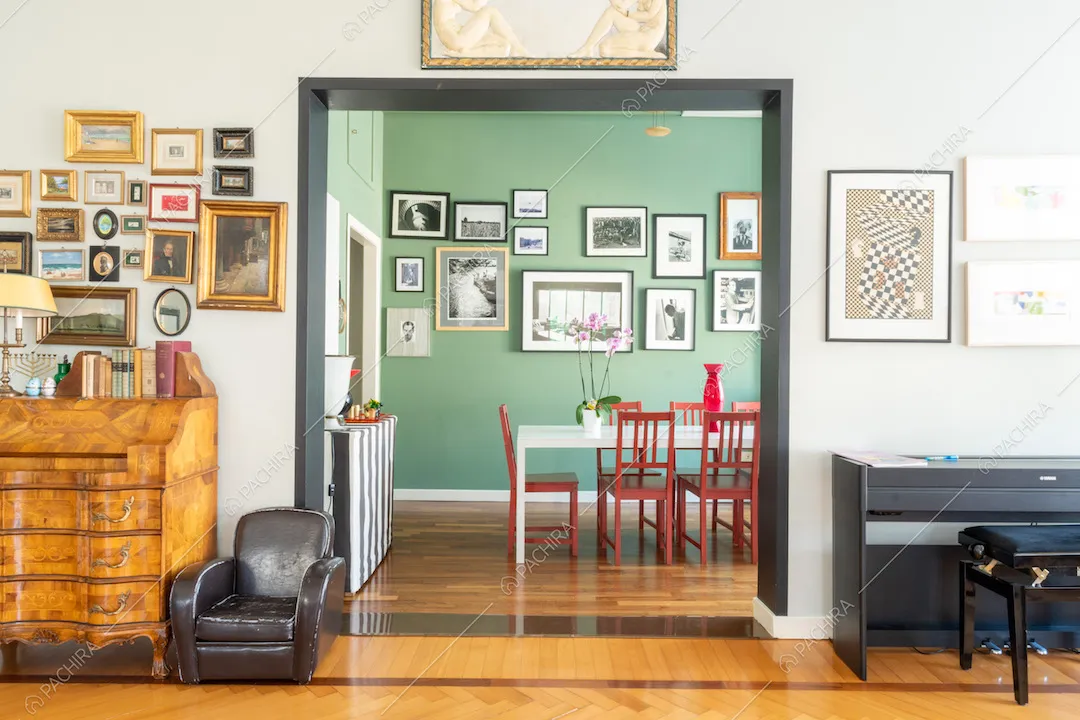 Vista sulla sala da pranzo dalle pareti verdi con pavimento in parquet, tavolo bianco e sedie rosse