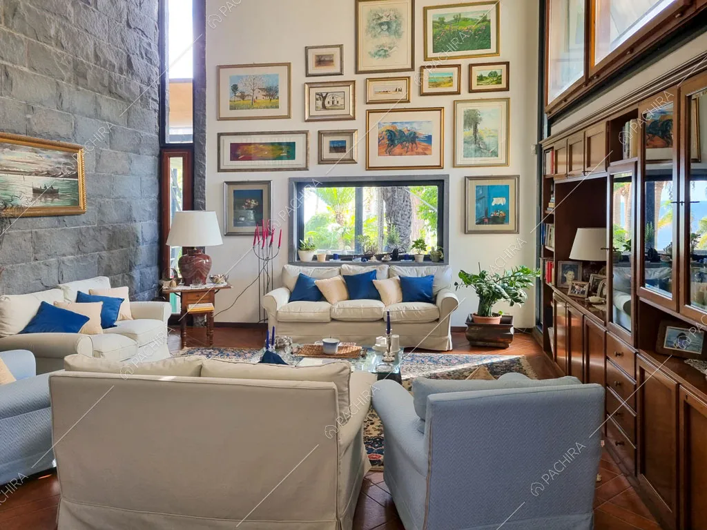 Salotto con divani e poltrone bianchi, credenza in legno e parete in pietra a vista