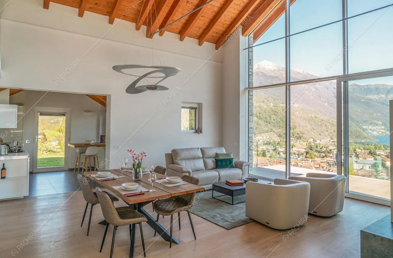Soggiorno dalle pareti bianche, soffitto con travi in legno a vista e ampia vetrata con porta-finestra