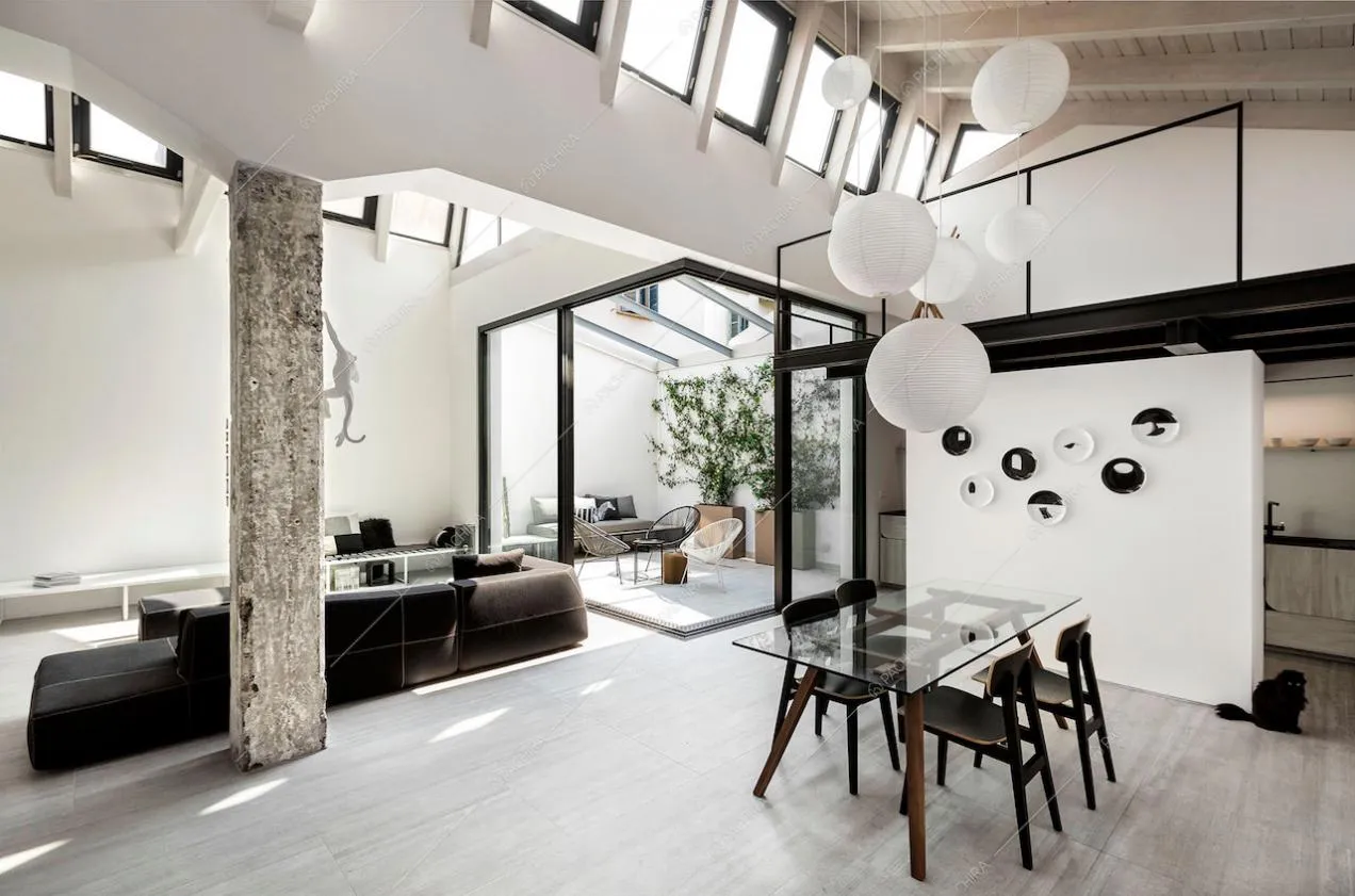 Sala con tavolo da pranzo con piano da lavoro in vetro, divano nero e giardino d'inverno