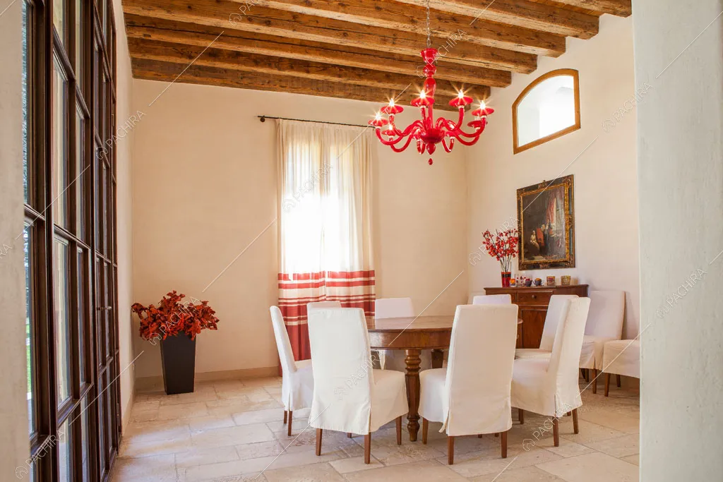 Sala con porta-finestra in metallo nero, tavolo da pranzo in legno e soffitto con travi a vista