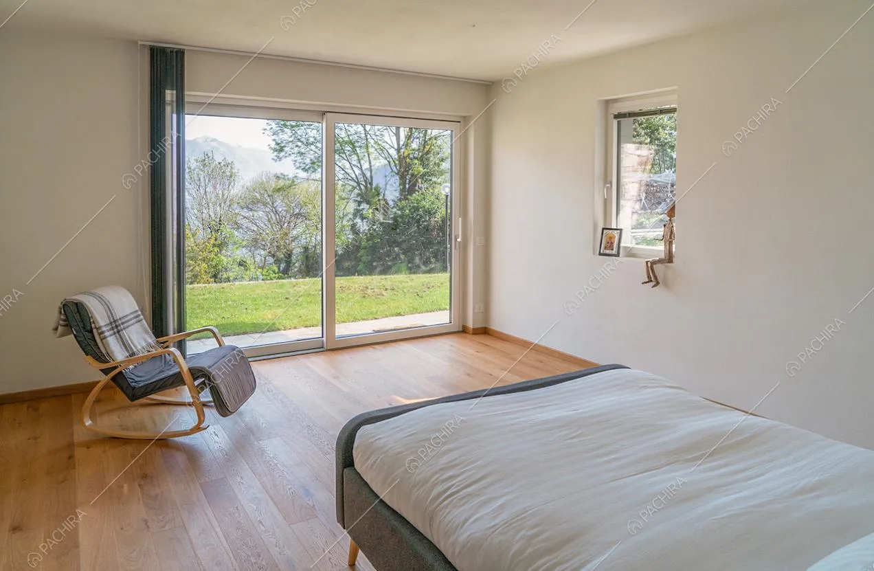 Porta-finestra scorrevole illumina la camera da letto matrimoniale con pavimento in parquet e pareti bianche