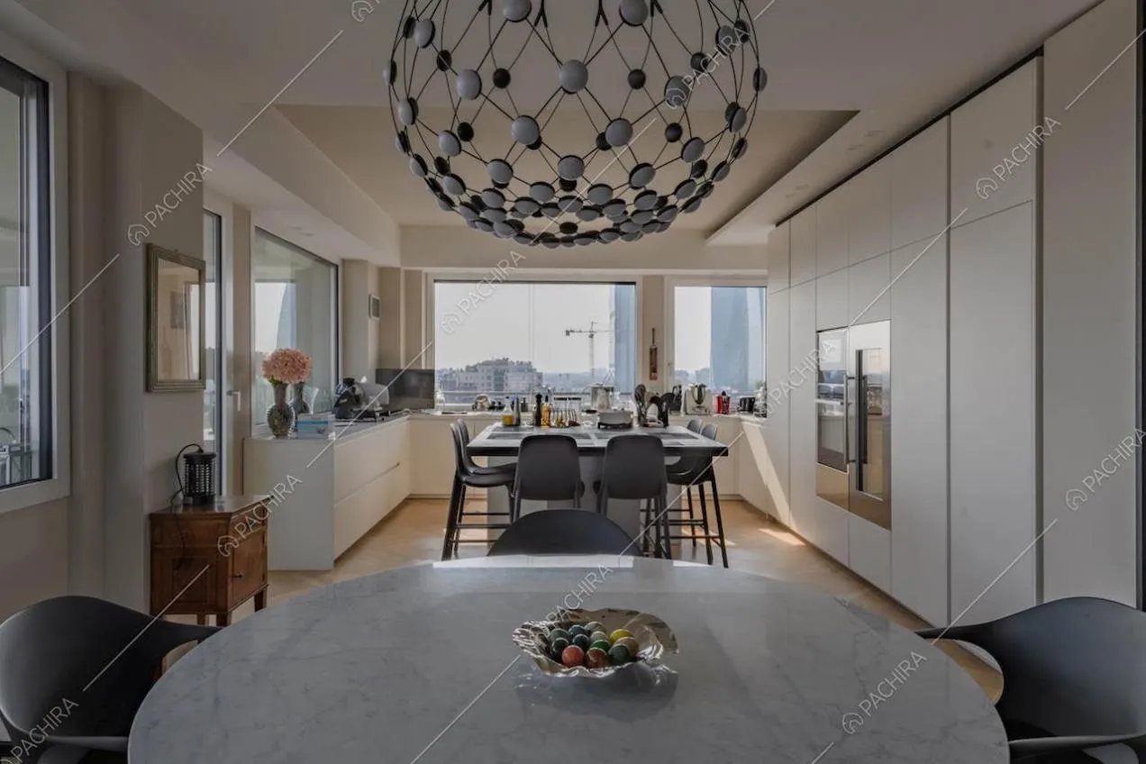 Dal tavolo da pranzo rotondo vista sulla cucina con isola e sugli armadi a muro