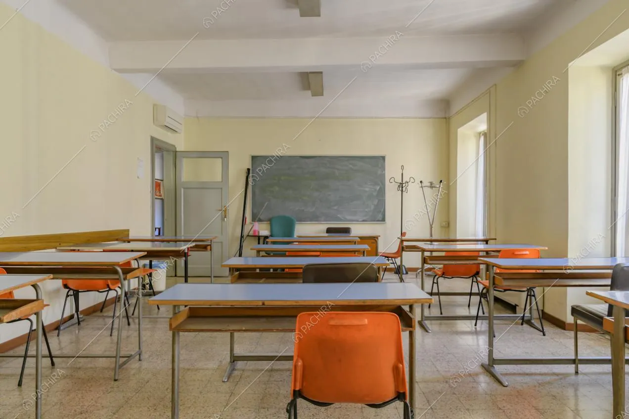 Aula dalle pareti gialle con pavimento in piastrelle, lavagna nera e porta verde