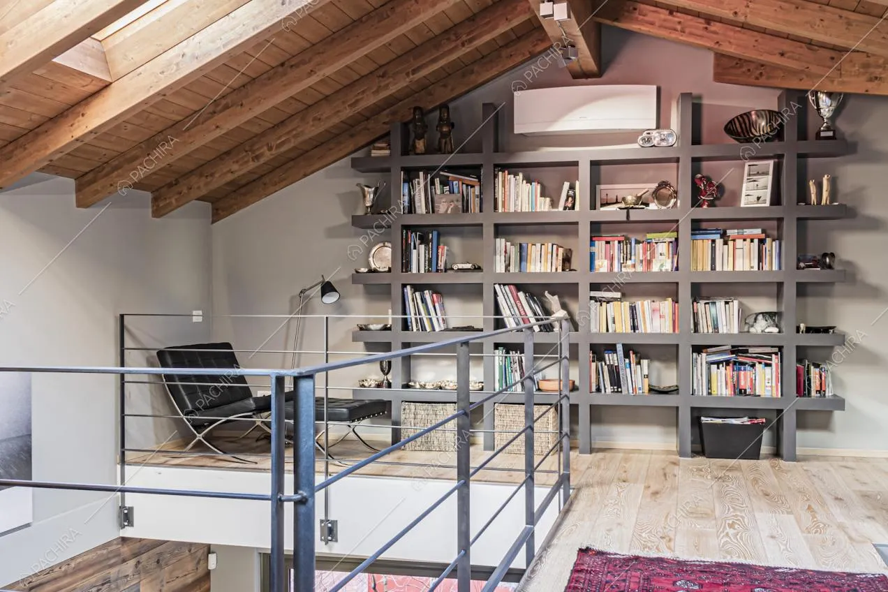 Libreria piena di volumi sotto alle travi in legno del sottotetto