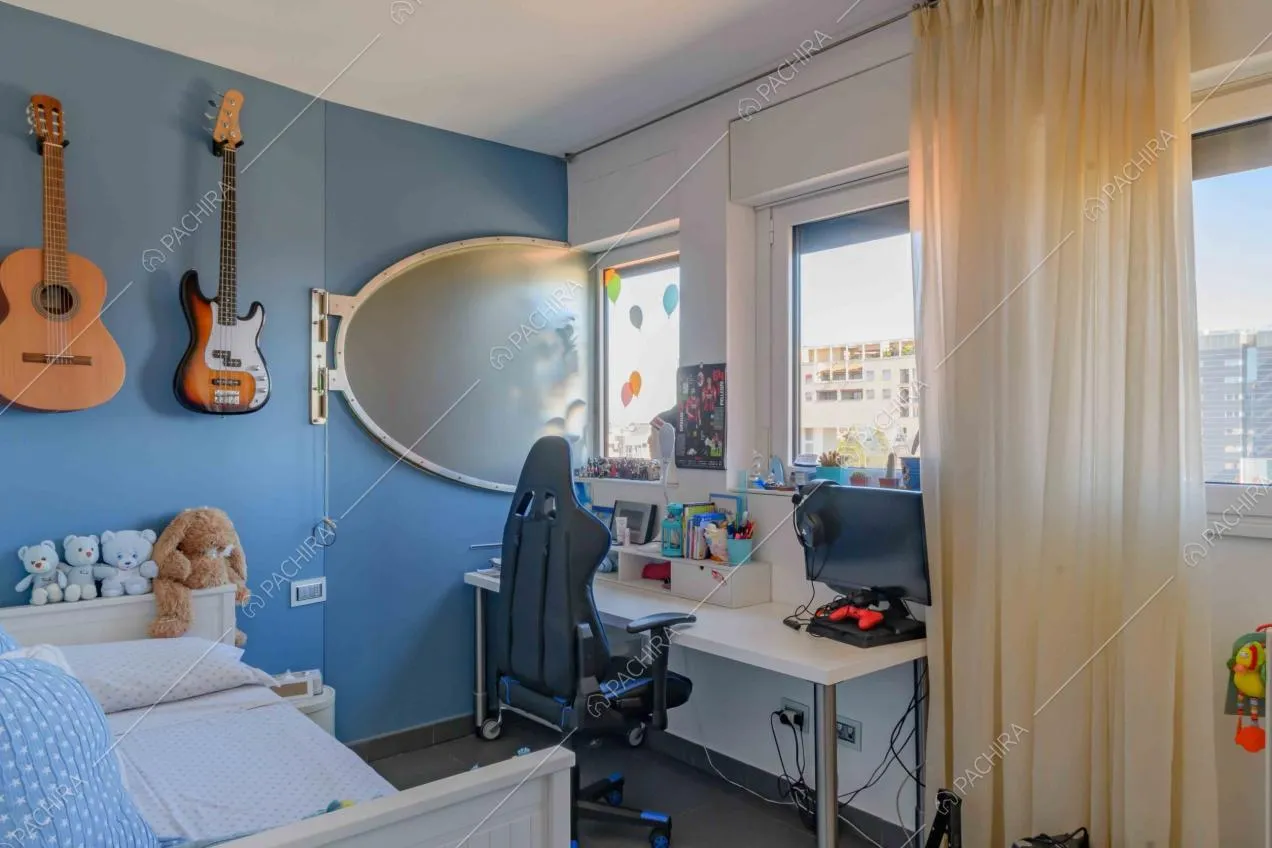 Camera da letto dalle pareti azzurre, con scrivani a bianca e vista sullo skyline