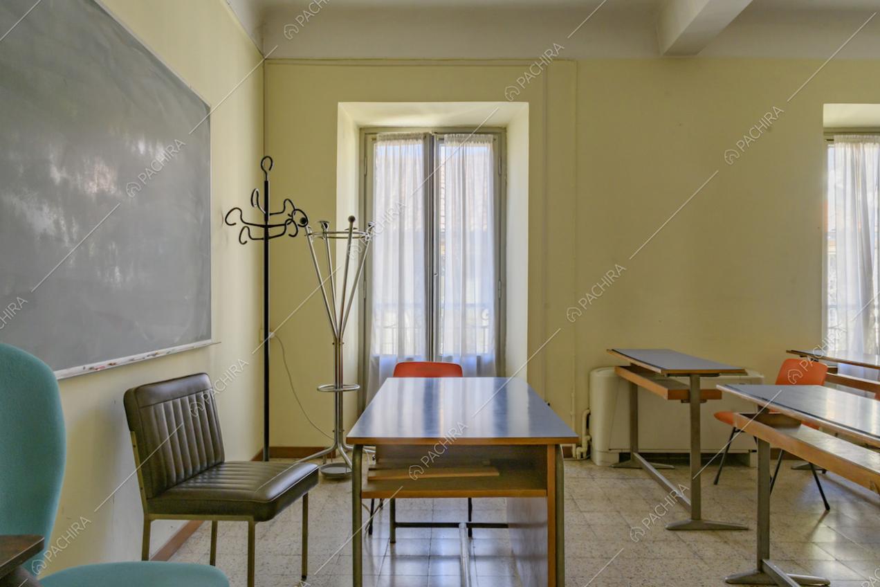 Aula dalle pareti gialle con cattedra, banchi, ampia lavagna nera e pavimento in piastrelle