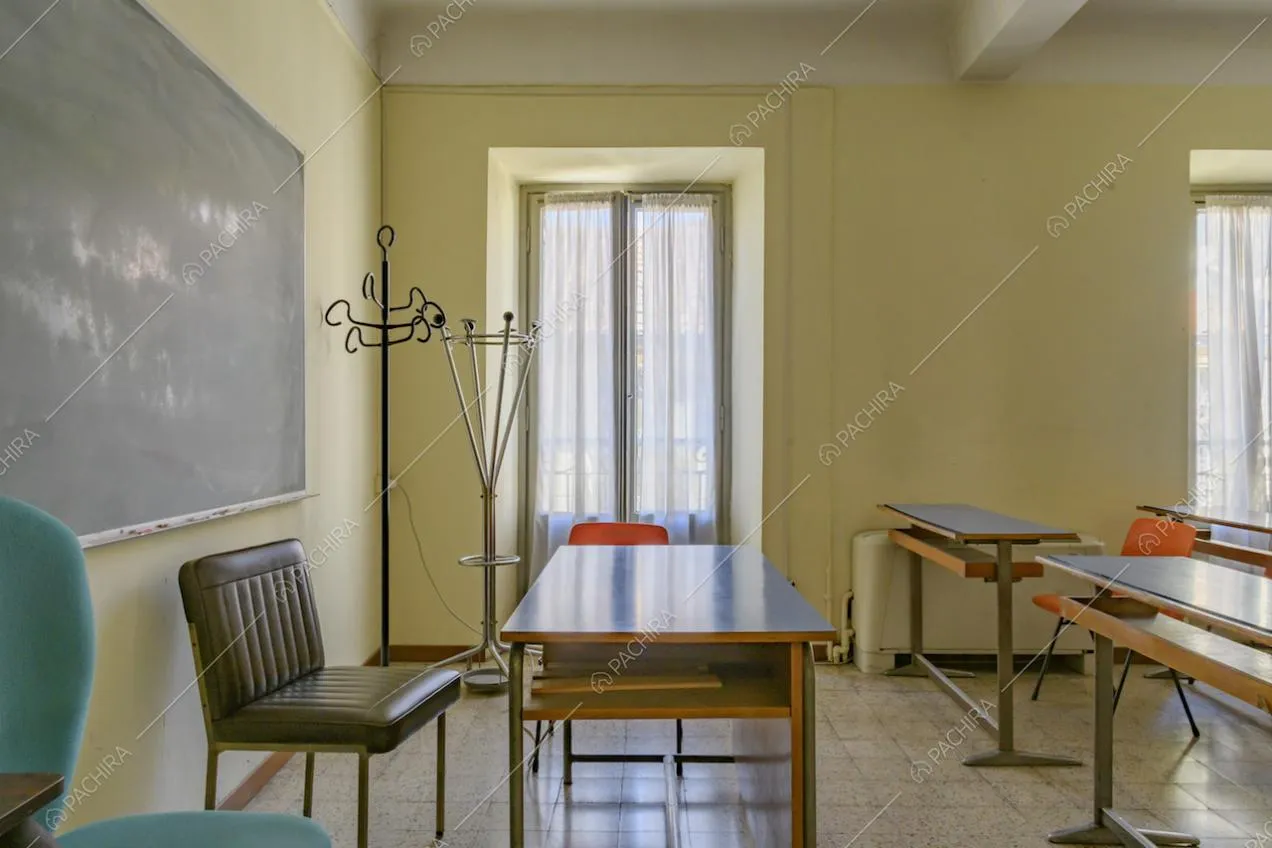 Aula dalle pareti gialle con cattedra, banchi, ampia lavagna nera e pavimento in piastrelle
