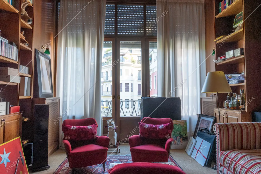 Poltrone rosse e divano nella biblioteca con porte-finestre per accedere al balcone