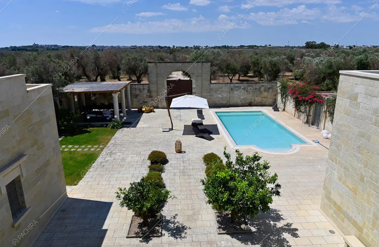 Dal tetto della villa vista sul cortile con piscina, ombrellone bianco e gazebo