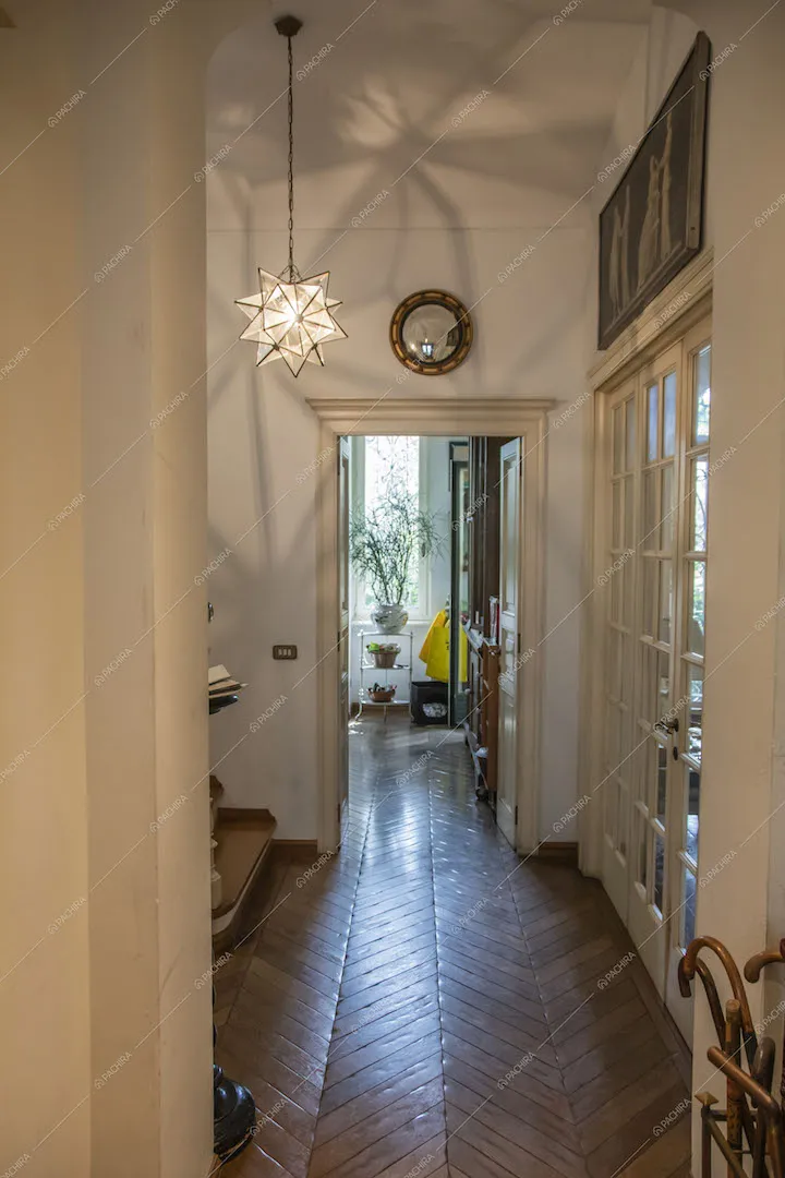 Luminoso corridoio con pareti bianche, pavimento in parquet a spina di pesce e lampadario di design