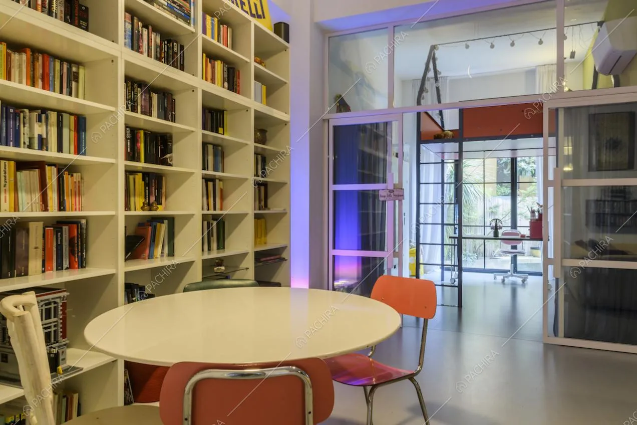 Salotto con tavolo, libreria e vista su camera da letto con porta scorrevole a vetri