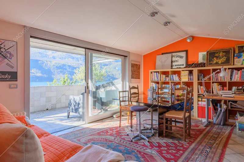 Salotto con parete rossa e porta-finestra scorrevole con vista sul lago