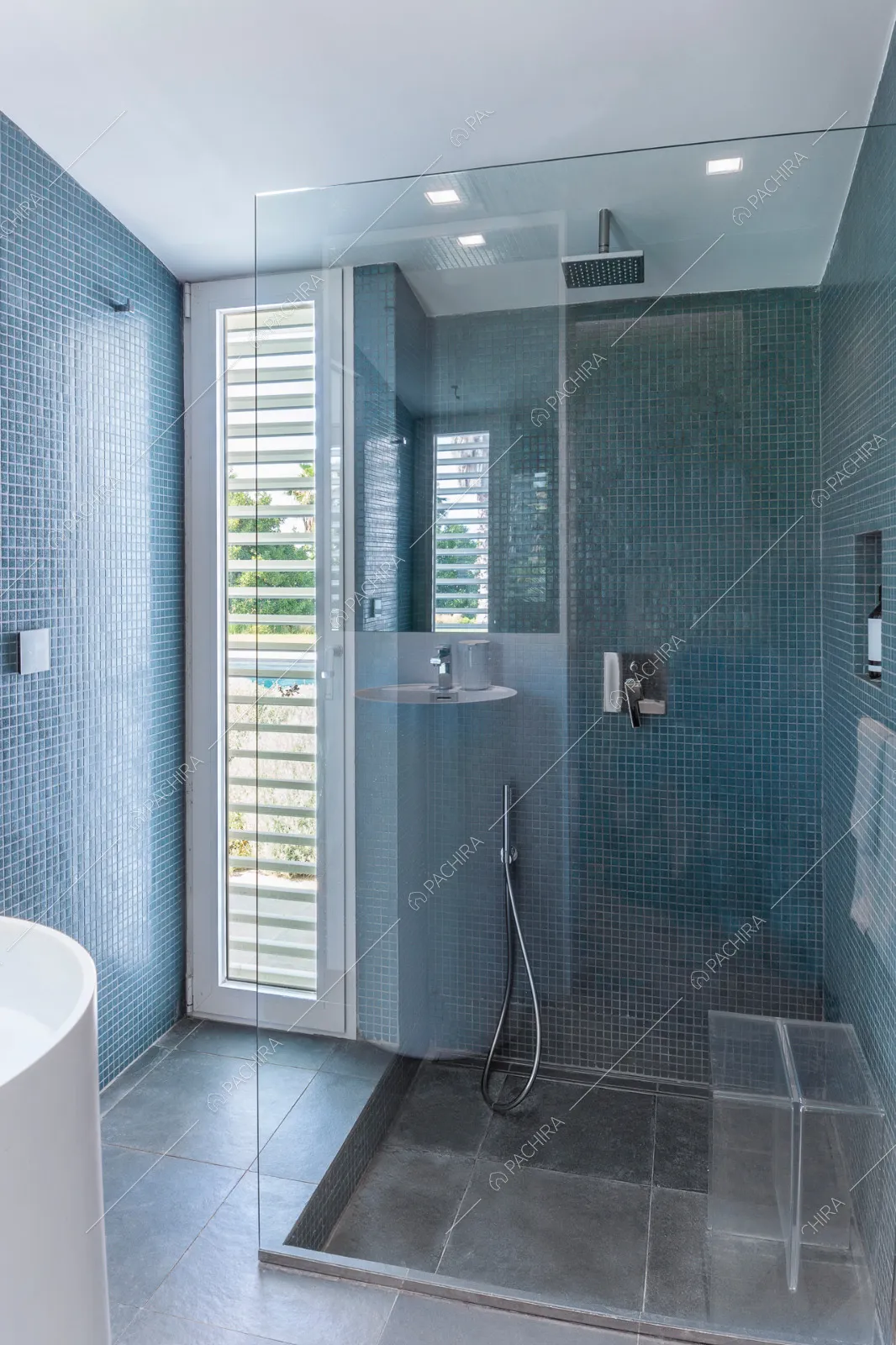 Bagno con piastrelle blu alle pareti e ampio box doccia con parete in vetro
