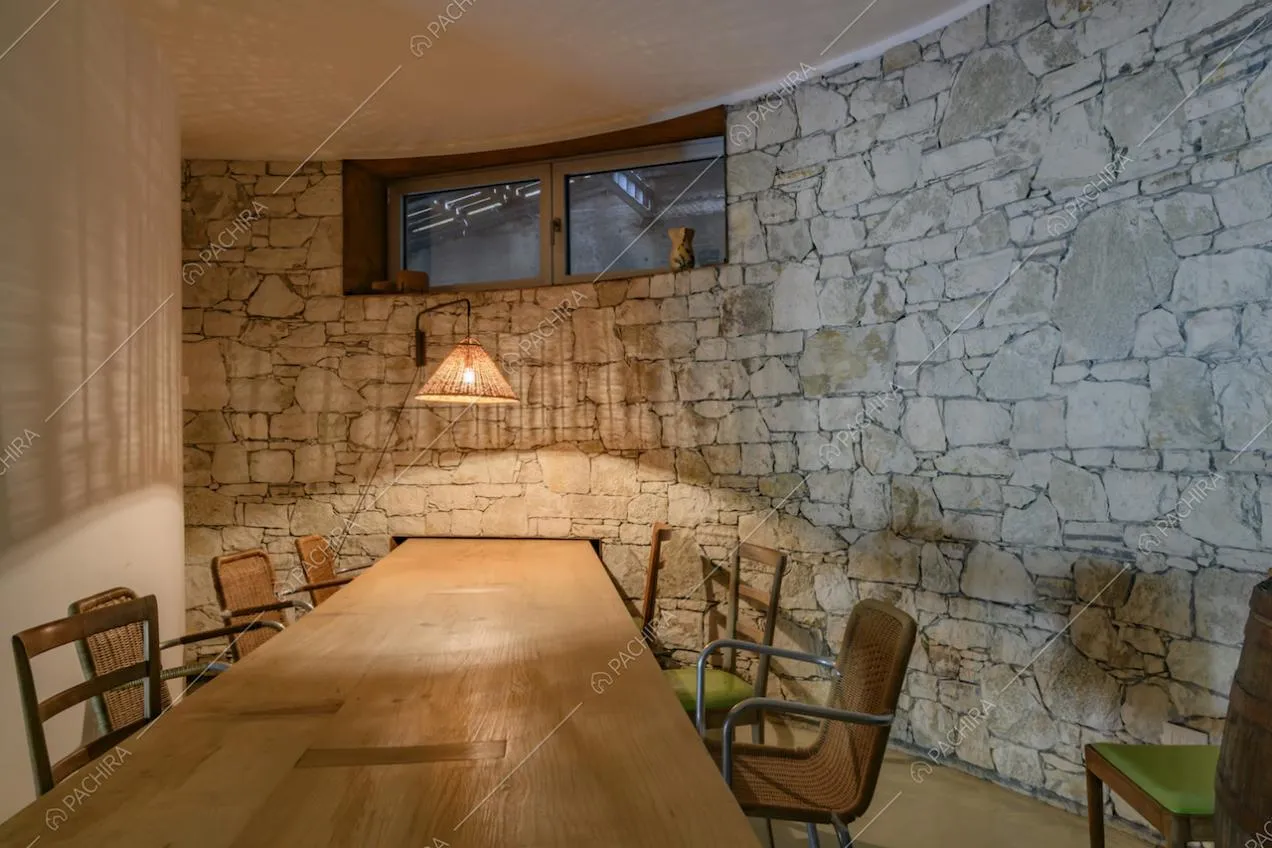 Tavolo da pranzo in legno nella sala con pavimento in cemento lisciato, pareti bianche e in pietra a vista