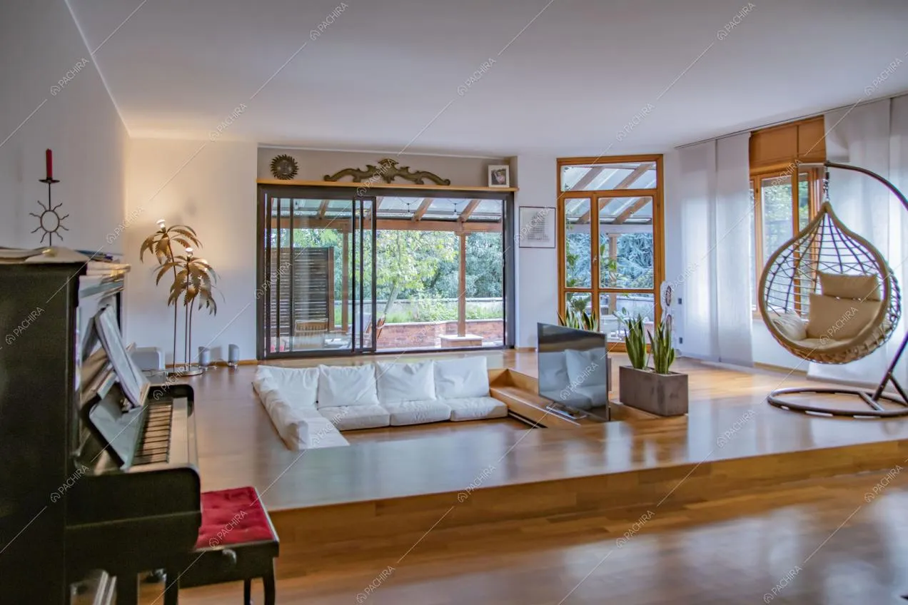 Vista sui divani bianchi e sul pianoforte nella zona living con grandi vetrate