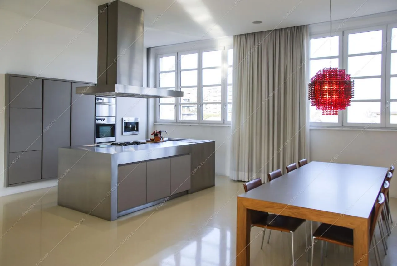 Vista sulla cucina a isola con piano di lavoro in acciaio e tavolo da pranzo