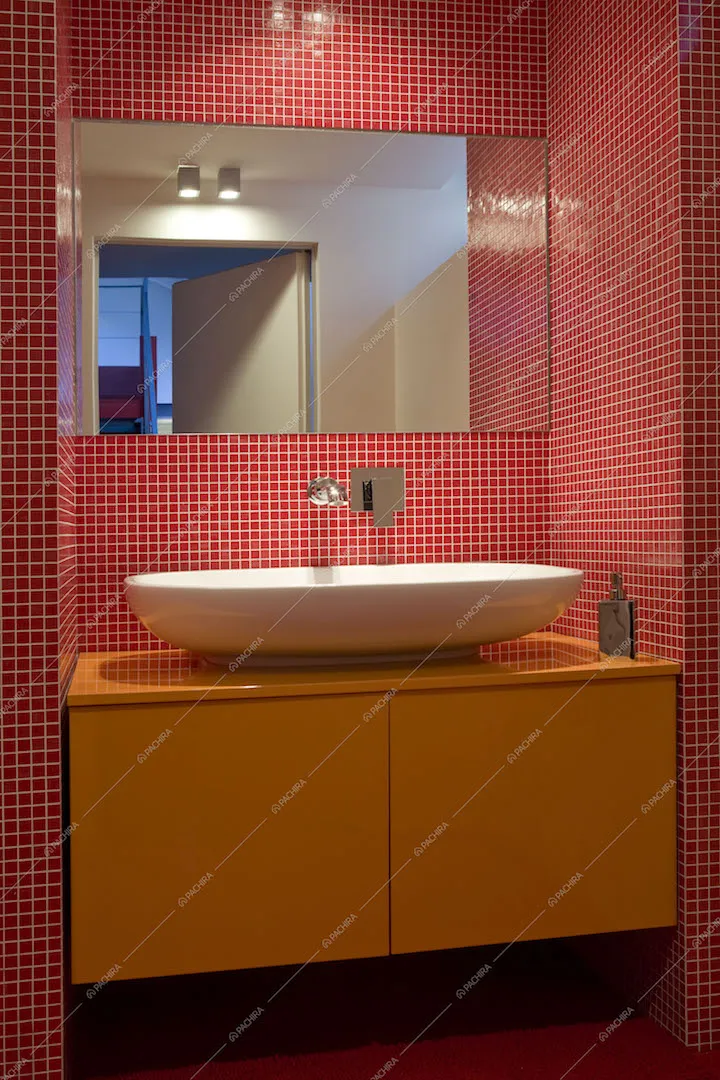 Lavandino del bagno su mobile sospeso arancione e parete a piastrelline rosse