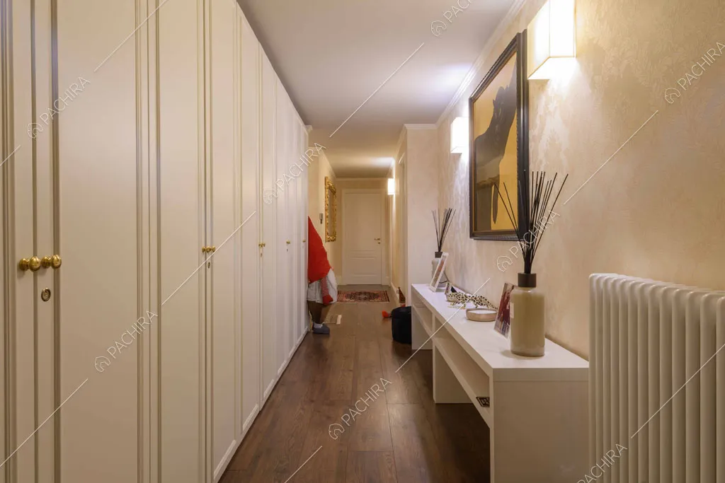 Lungo corridoio con carta da parati, armadi a muro bianchi e pavimento in parquet