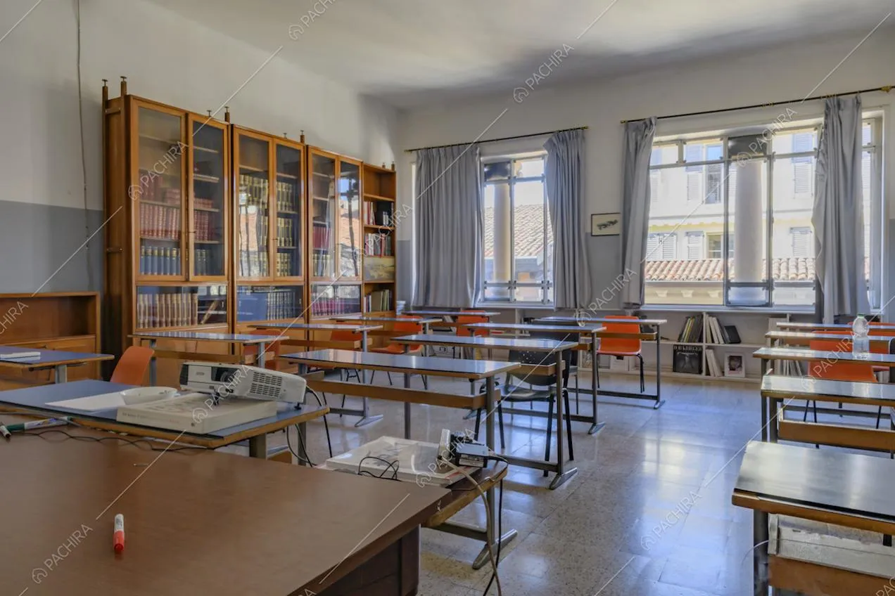 Ampia aula con libreria in legno e vetro, vetrate che illuminano lo spazio e numerosi banchi