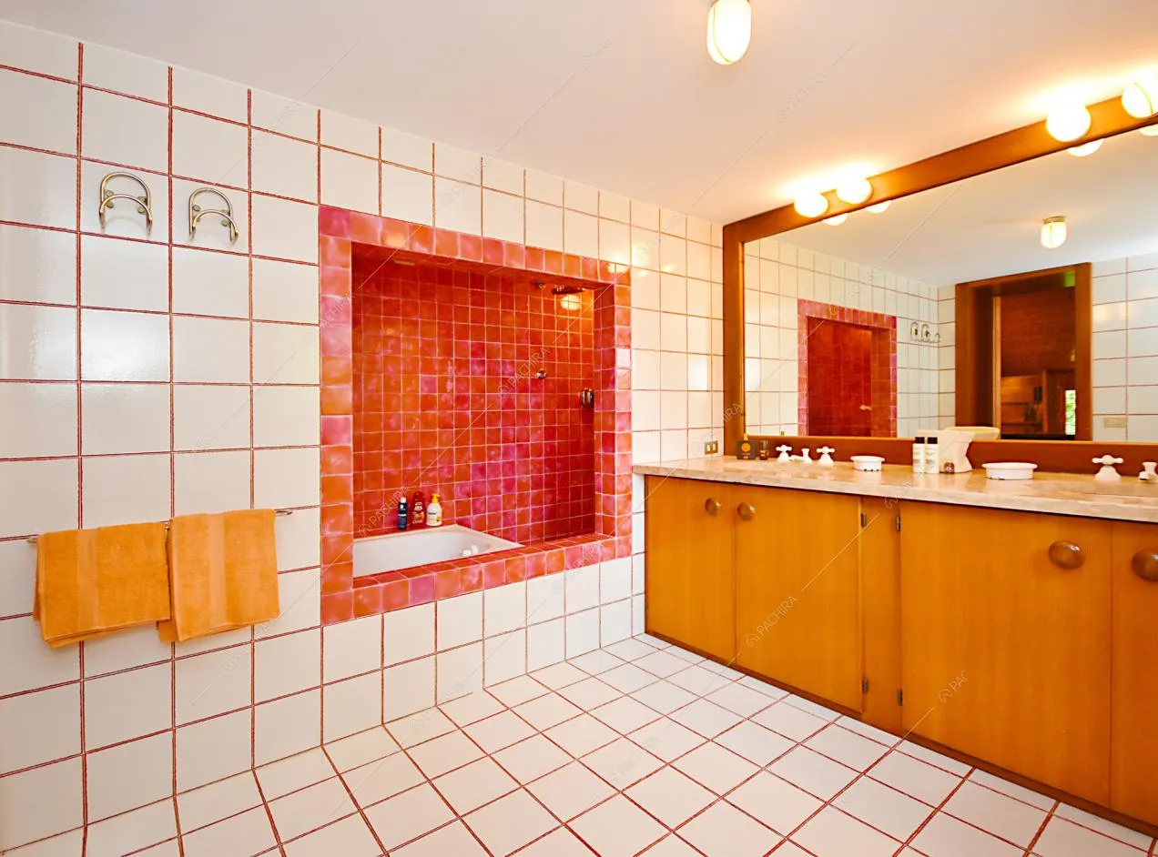 Bagno spazioso rivestito con piastrelle bianche, grande specchio e mobili in legno