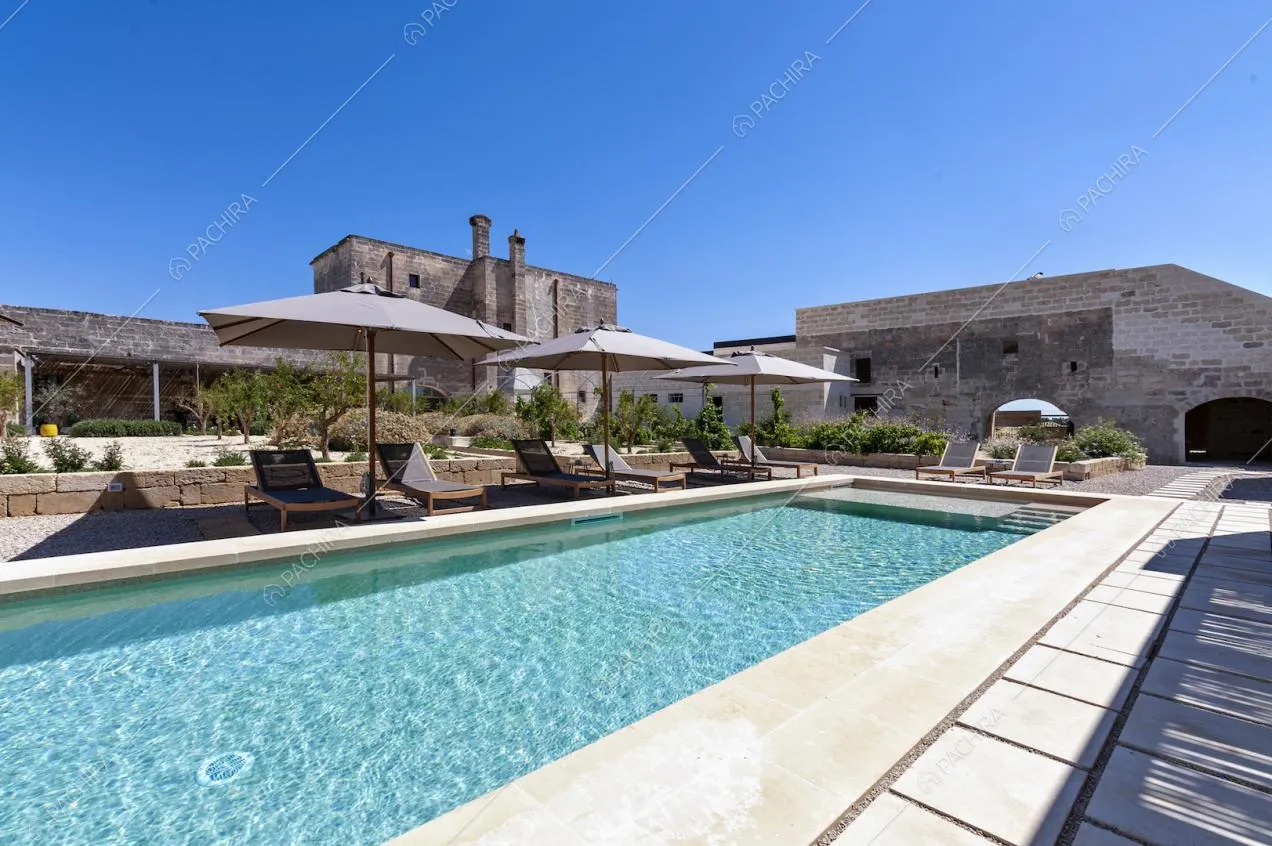 Grande piscina rettangolare e area relax nel cortile privato della masseria