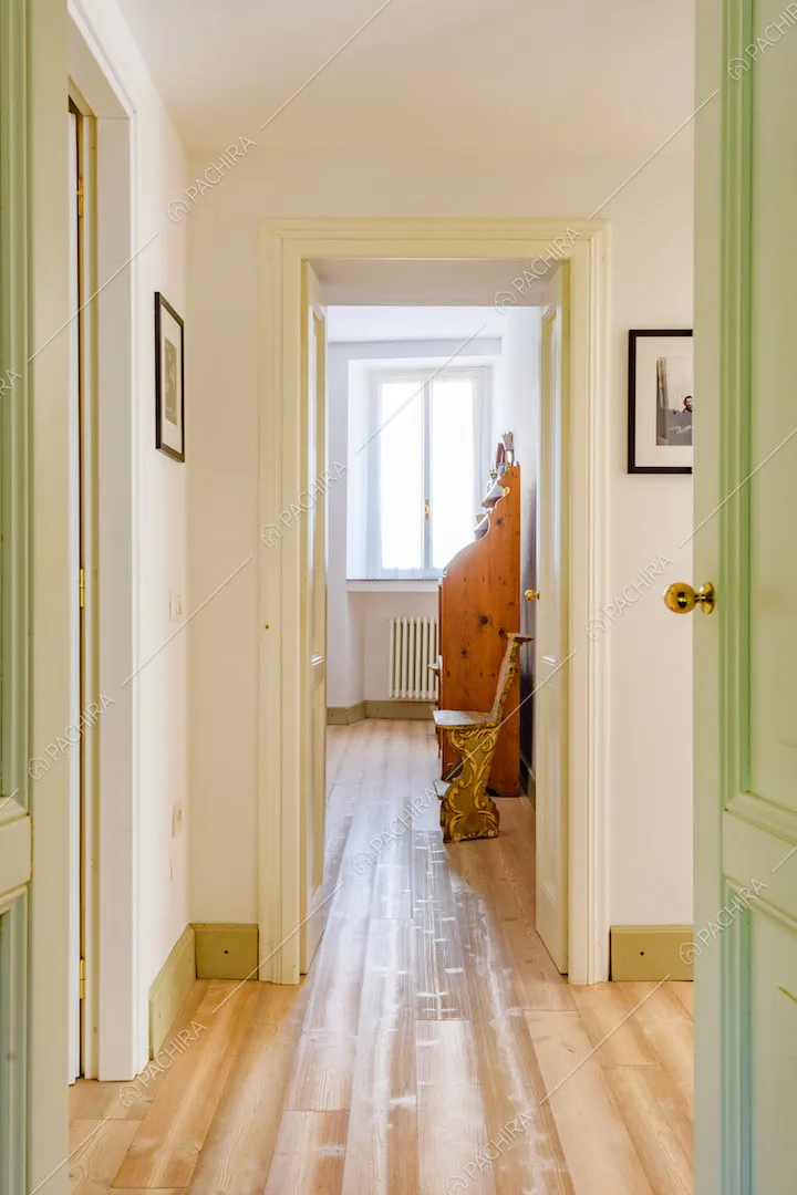 Corridoio con pareti bianche, porte verdi con boiserie e pavimento in parquet